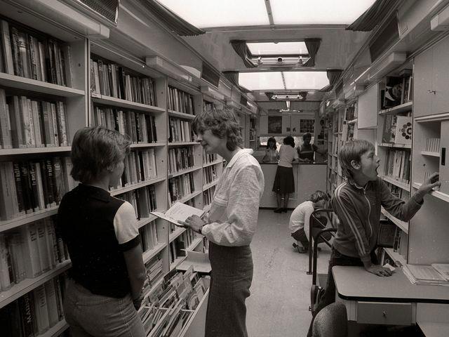 Innenansicht der Fahrbibliothek 1979, zwei Personen sind im Gespräche, eine weitere Person sucht im Bücherregal